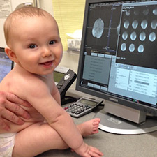 baby in front of computer screen with brain scan images on it